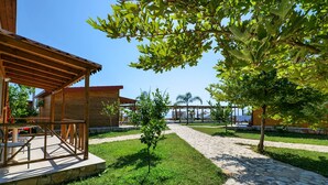 A covered outdoor area with a stone pathway, a small tree, and a building with a red roof. - Bunec Beach Resort (Lukovë)