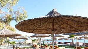 A beachside area with wooden lounge chairs and thatched umbrellas. - Bunec Beach Resort (Lukovë)