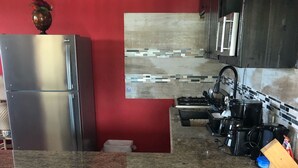 Cozinha com parede vermelha, geladeira de aço inoxidável, painel de azulejos, fogão a gás e dois bancos.