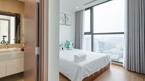 Moderni hotellihuone, jossa on suuri sänky, näköala kaupunkiin sekä kylpyhuone, jossa on peili ja pesuallas.