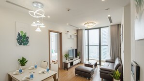 Moderni olohuone, jossa on sohva, kahdelle katettu ruokapöytä, televisio ja suuri ikkuna, jossa on verhot.