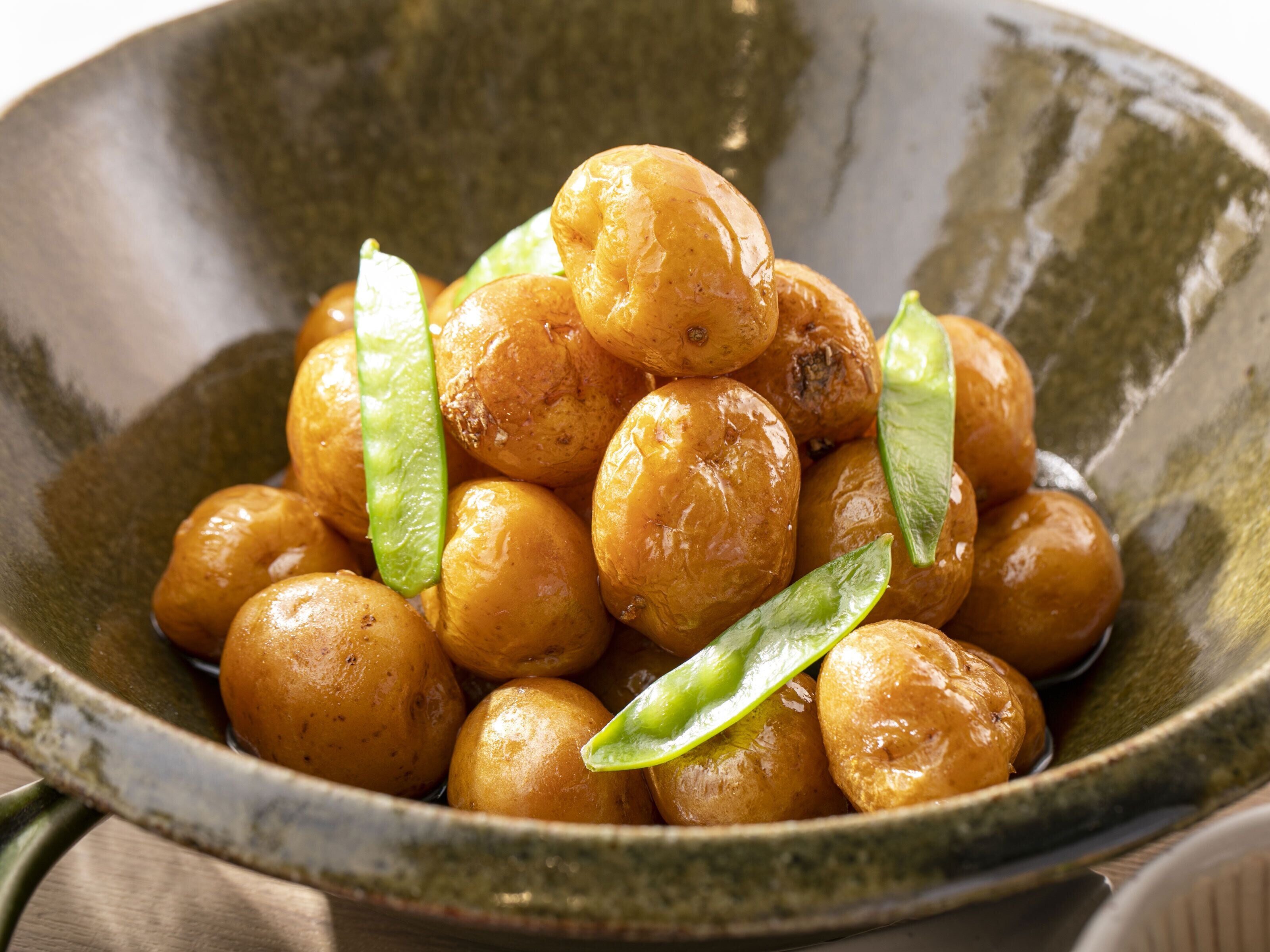 A bowl of golden-brown roasted potatoes garnished with green chili slices.