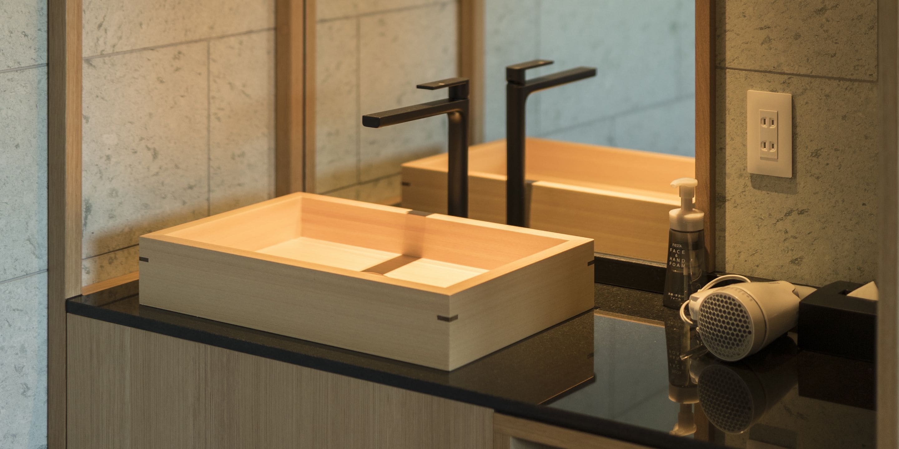 Ein modernes Badezimmer mit einem Holzwaschtisch, einem schwarzen Wasserhahn und einem Fön auf der Ablagefläche.