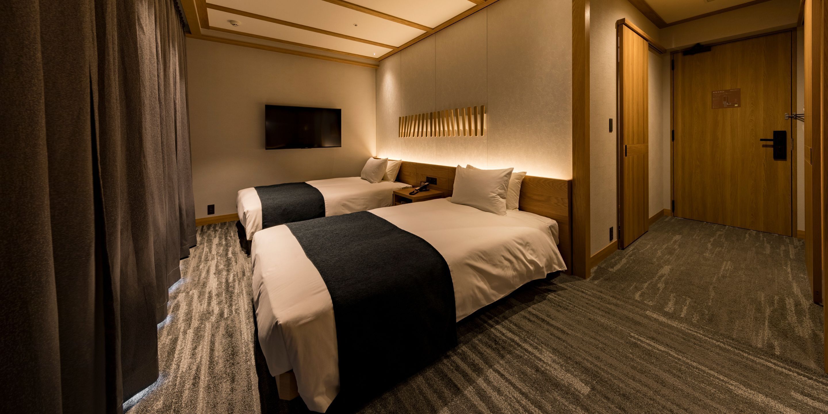 A hotel room with two beds, a flat-screen TV mounted on the wall, and a wooden door.