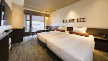 Habitación de hotel con dos camas, un escritorio, una silla, un televisor y un ventanal con vistas a la ciudad.