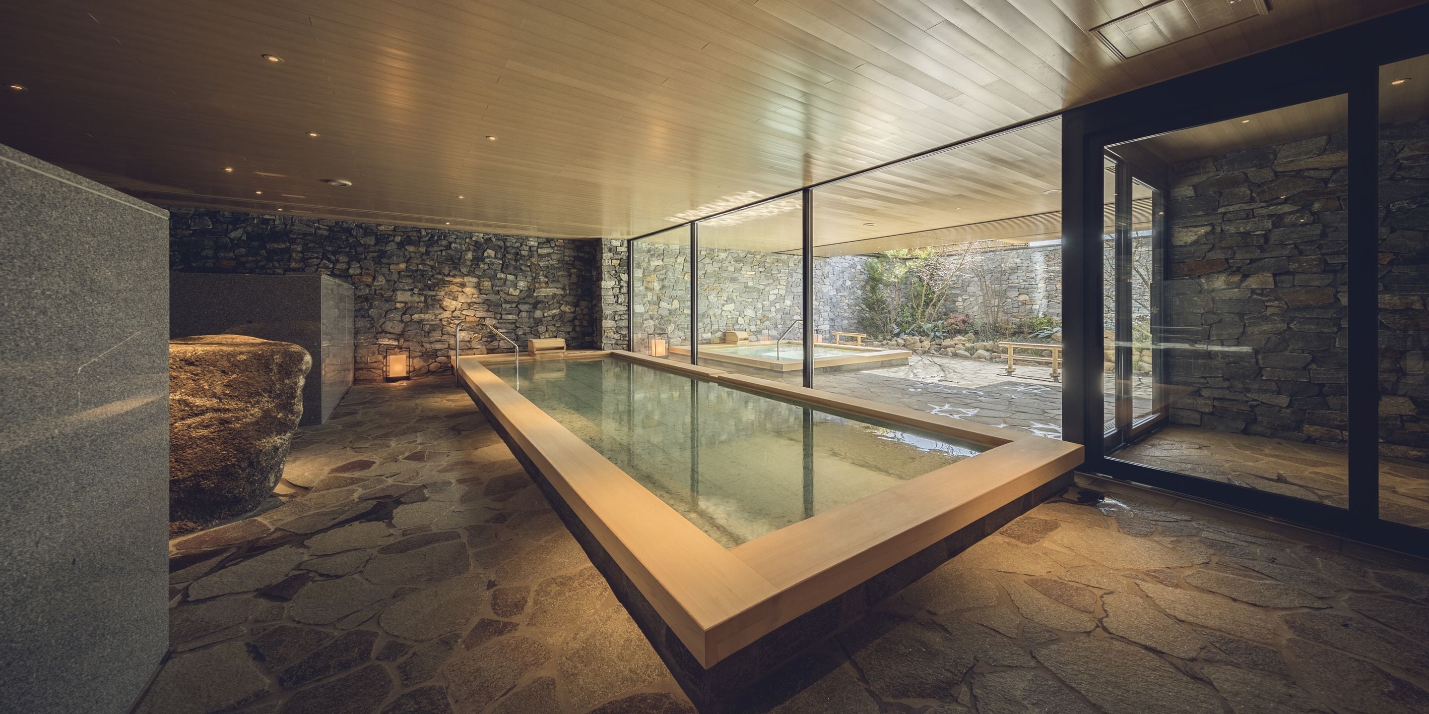 A modern indoor pool area with stone walls and a glass enclosure.
