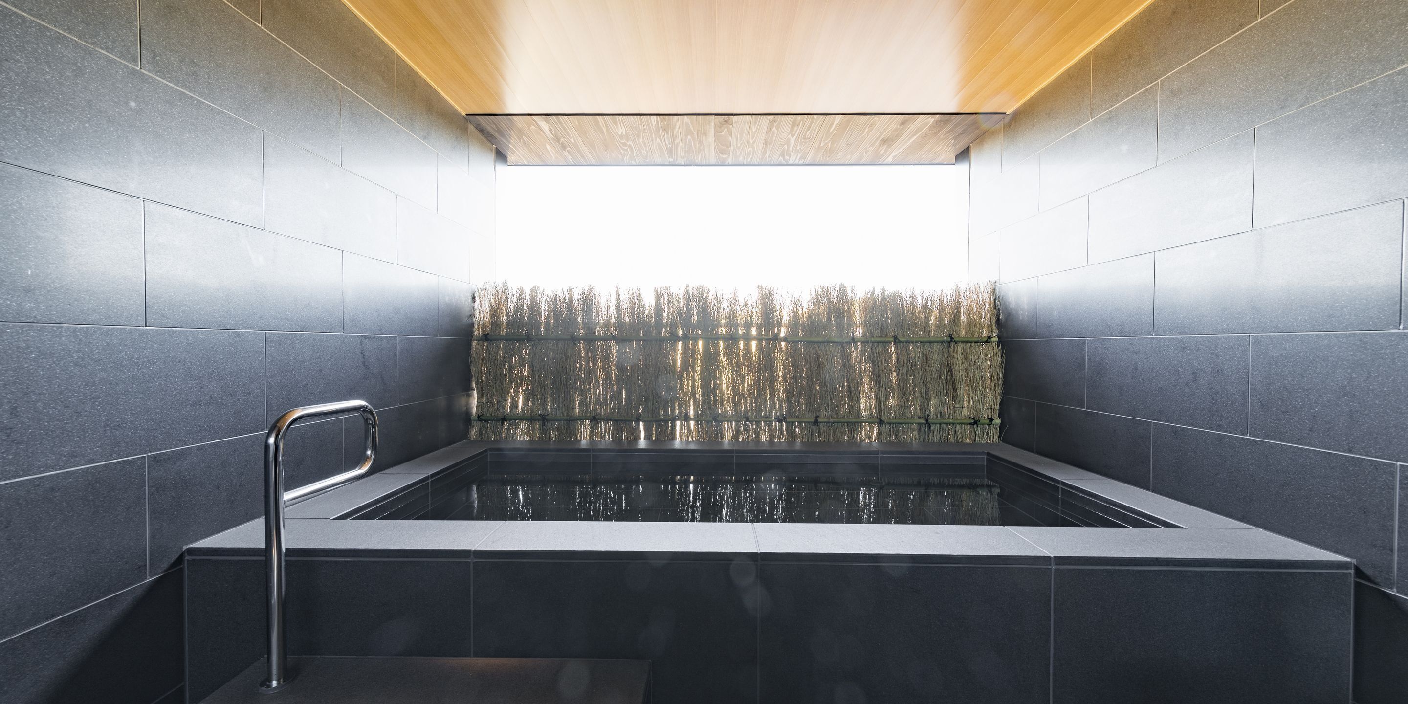 A modern spa with a rectangular hot tub, tiled walls, and a wooden ceiling.