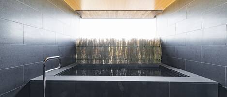 A modern spa with a rectangular hot tub, tiled walls, and a wooden ceiling.