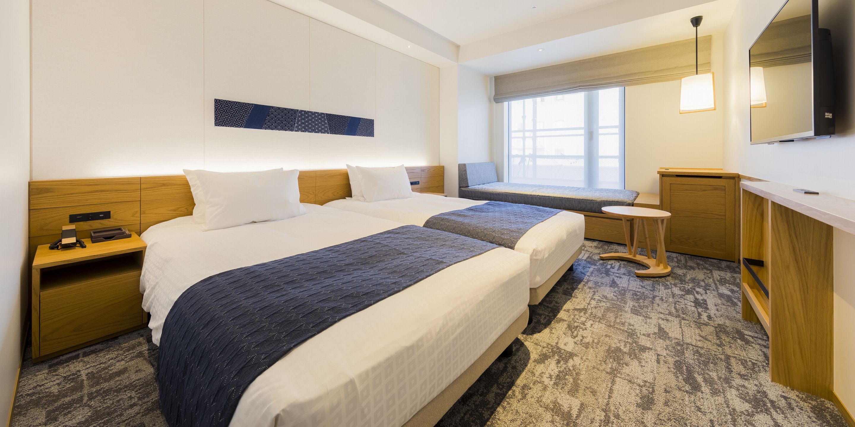 Habitación de hotel con dos camas, un pequeño rincón de estar junto a la ventana, un escritorio y una televisión.
