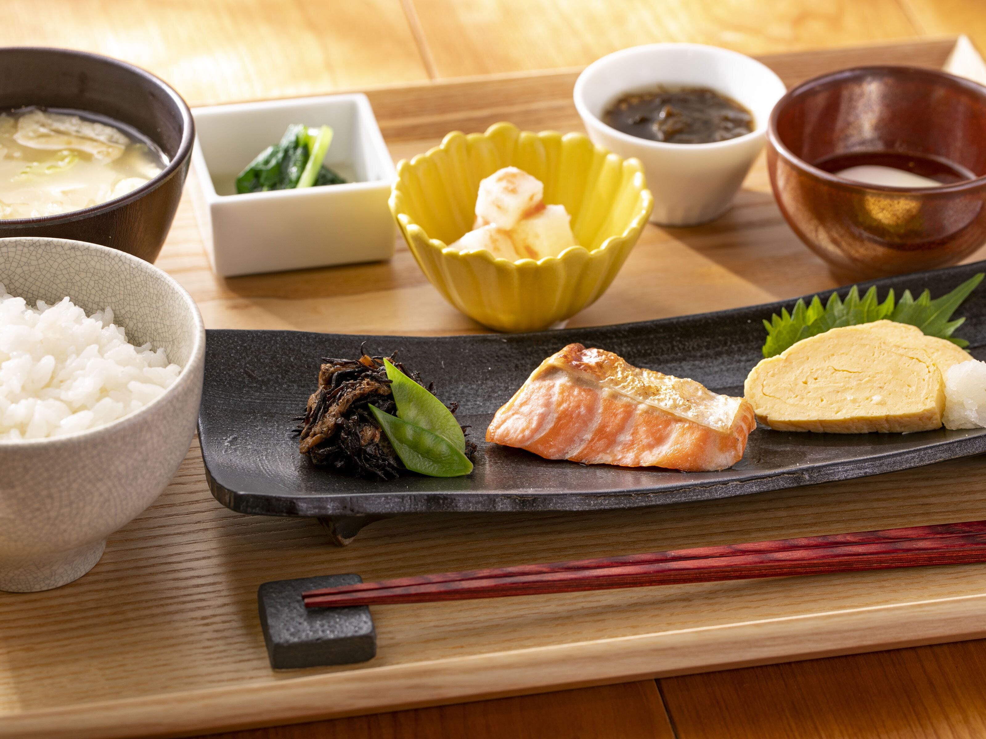 A traditional Japanese meal with rice, salmon, and tofu on a black plate, accompanied by soup and side dishes.