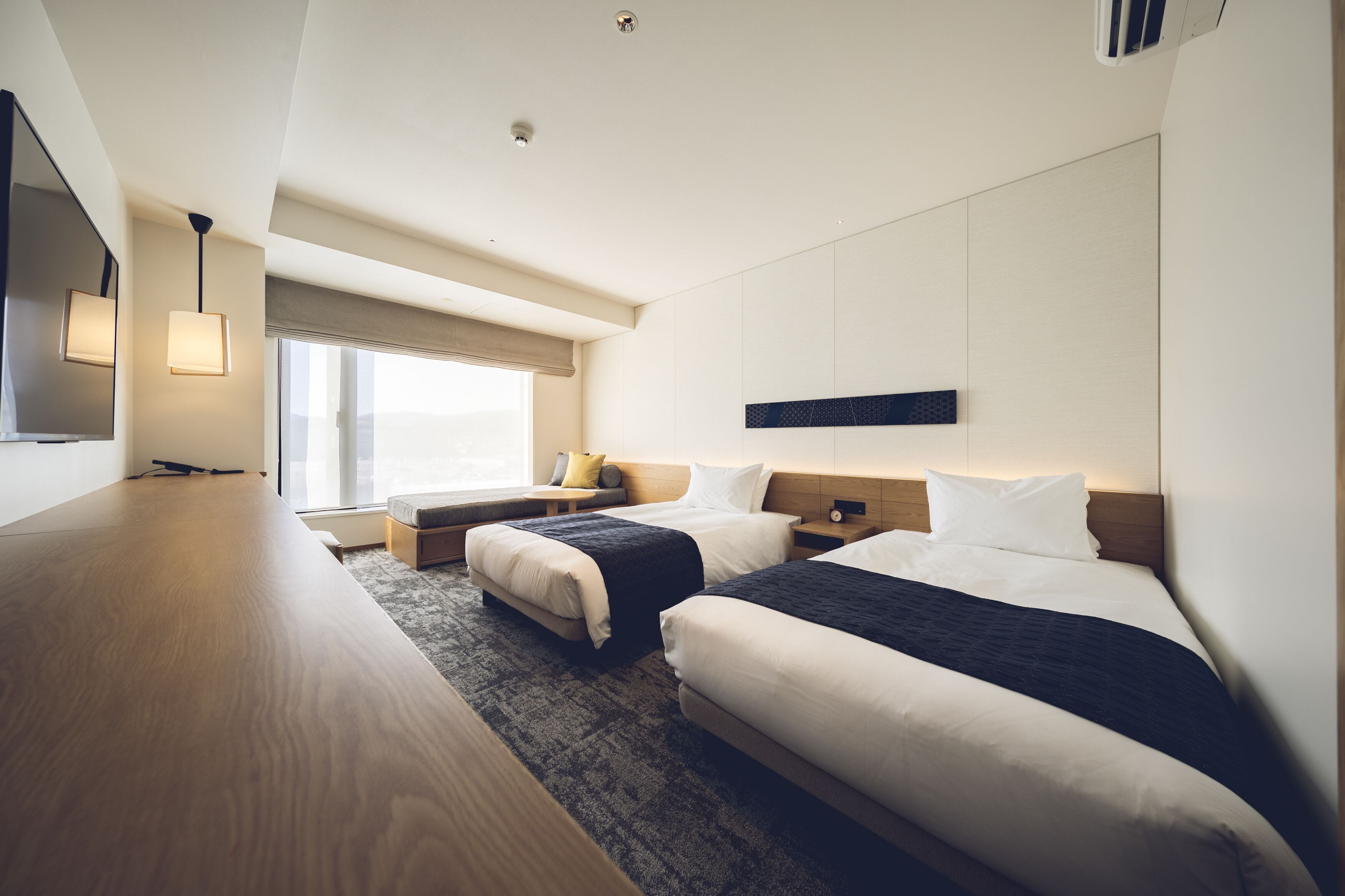 Ein modernes Hotelzimmer mit zwei Betten, einem Holztisch und einem großen Fenster.