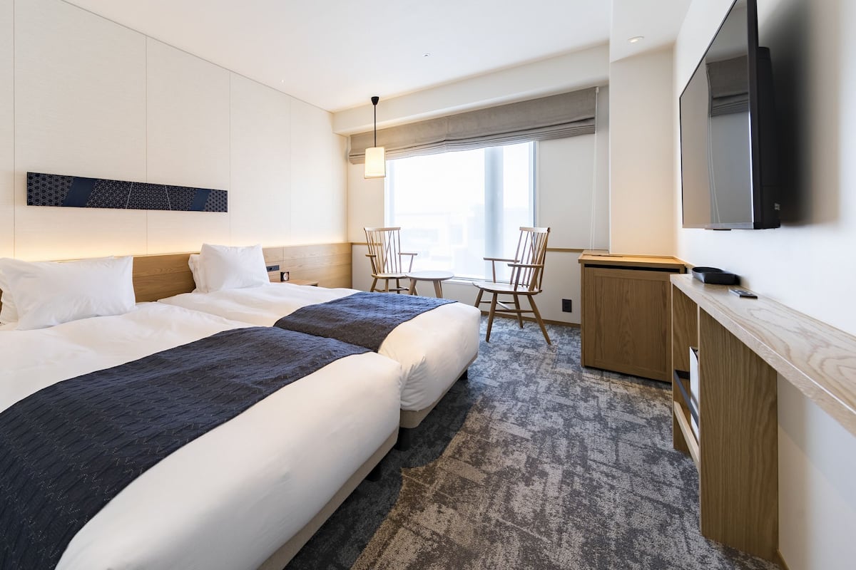 A hotel room with a large bed, bedside tables, a desk, a chair, and a TV mounted on the wall.
