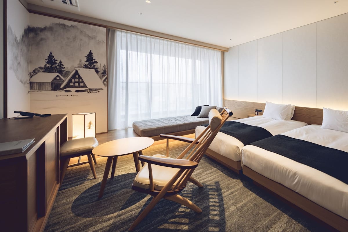 A modern hotel room with a large bed, a desk, a chair, and a small table.