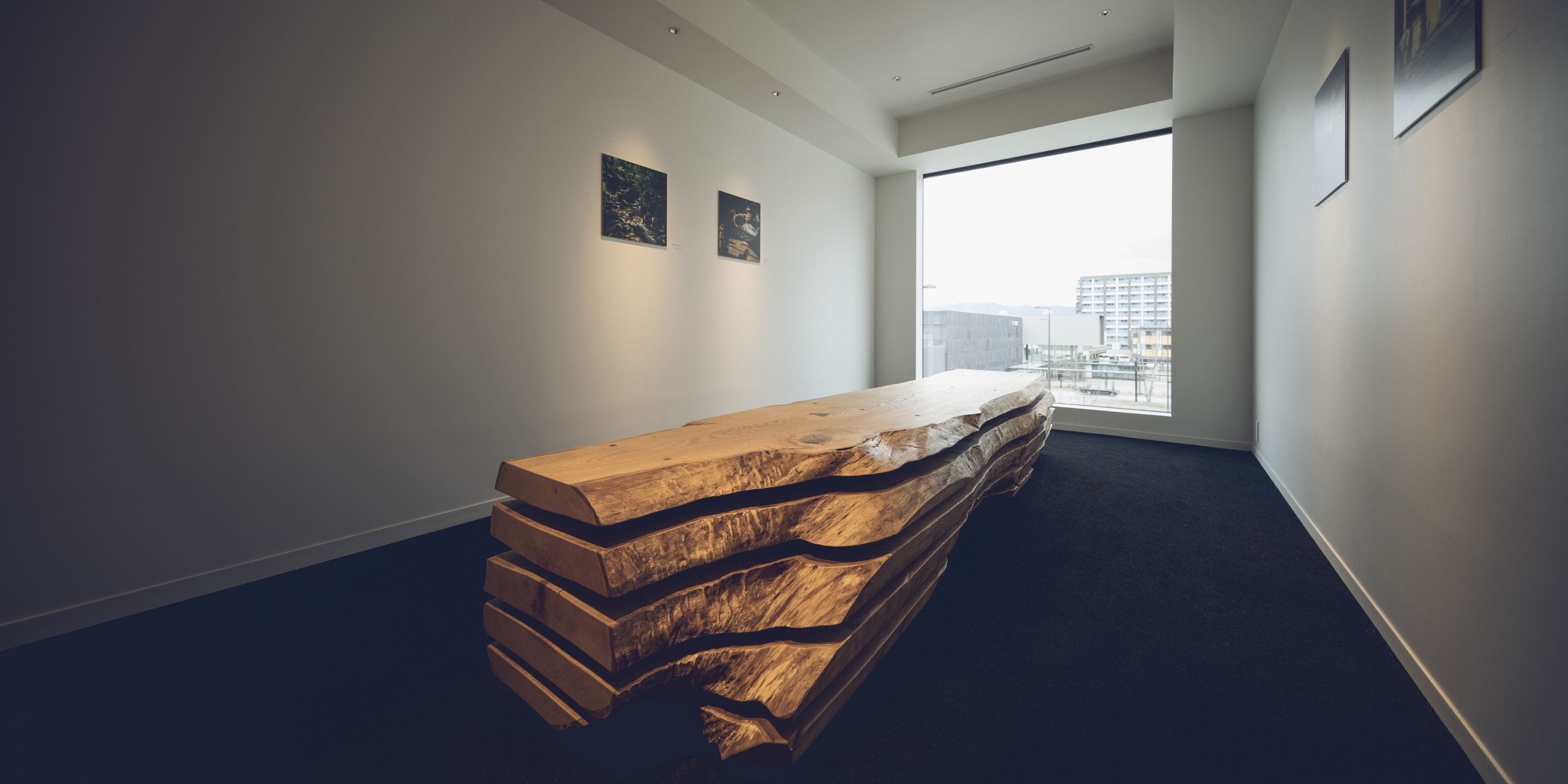 Un intérieur moderne avec un banc en bois, des œuvres d’art encadrées accrochées aux murs et une vue sur les bâtiments par une grande fenêtre.