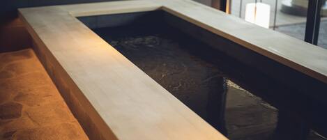 Un espace spa moderne doté d’un bain à remous bordé de pierres et d’un banc en bois.