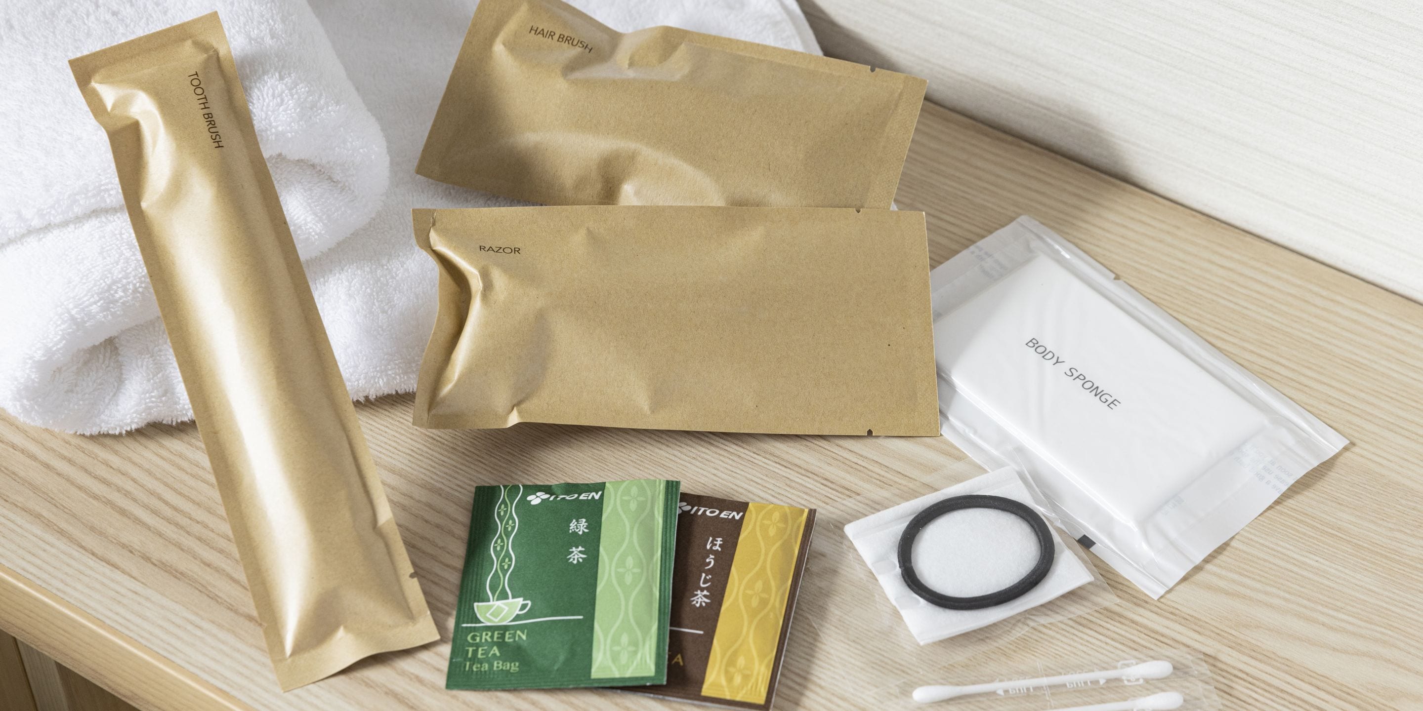 A wooden surface with various personal care items including a hair brush, razor, body sponge, green tea tea bag, and a toothbrush.