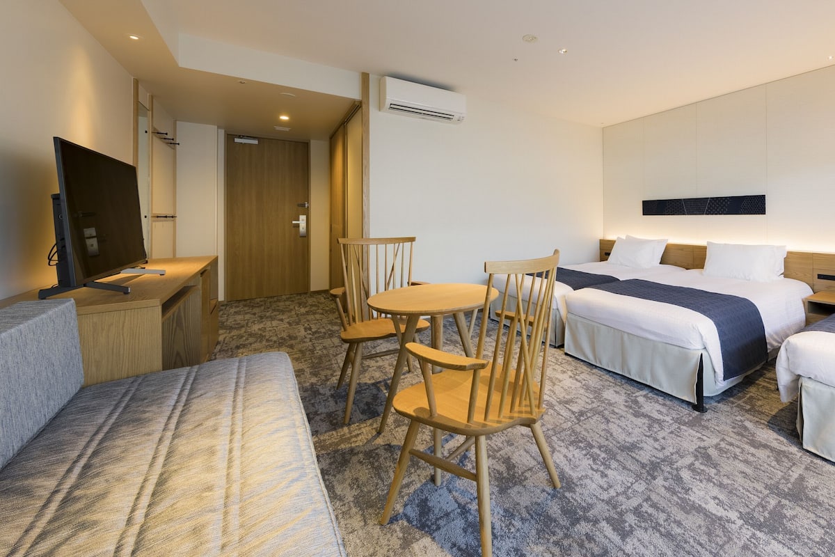 A hotel room with two beds, a desk with a chair, a TV, and a small table.