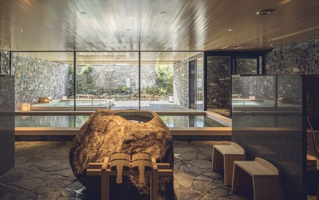 A spa area with a large rock centerpiece, stone walls, and a view of an outdoor pool.