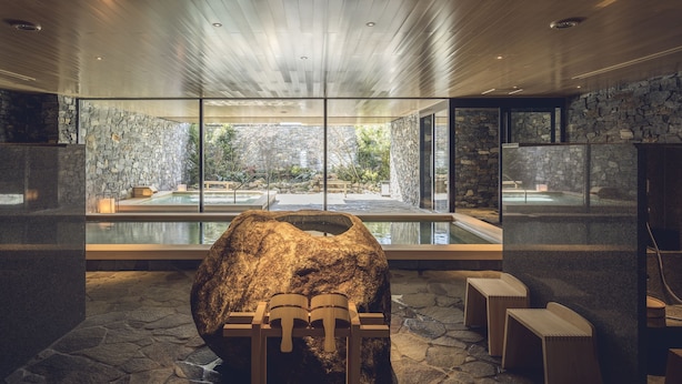 Un espace spa doté d’un grand rocher central, de murs en pierre et d’une vue sur une piscine extérieure.