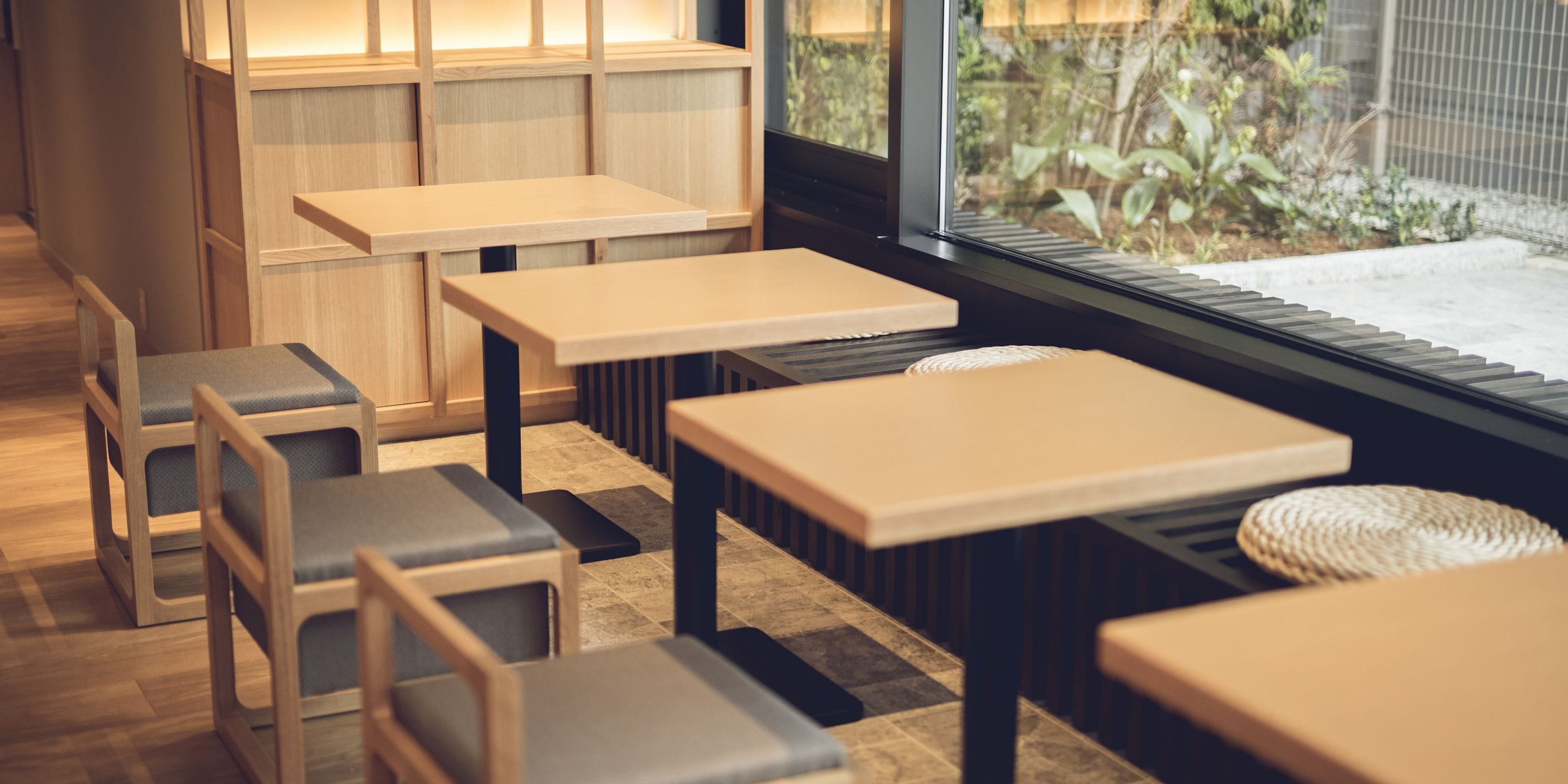 Ein modernes Interieur mit Holztischen und -stühlen, Blick auf Grünflächen und einem Fliesenboden.