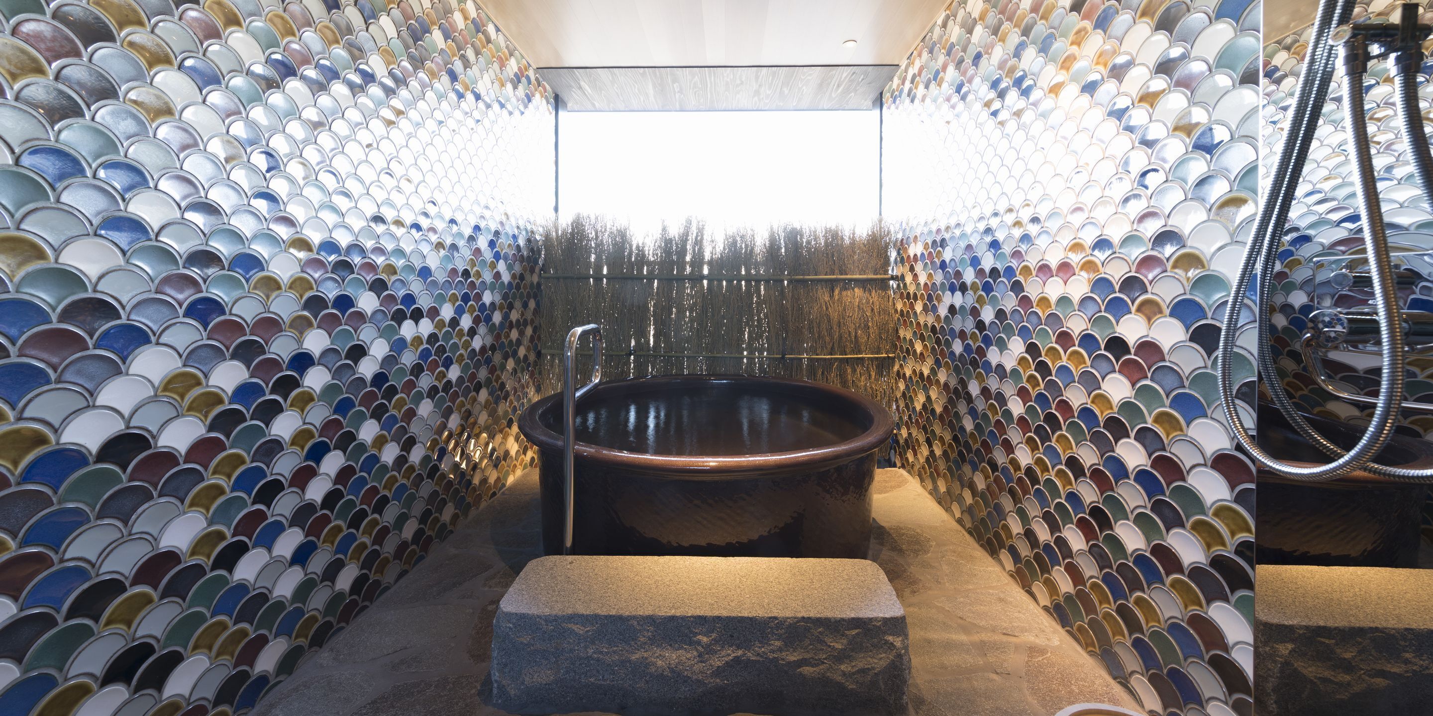 A bathroom with a large bathtub surrounded by a wall of colorful tiles.