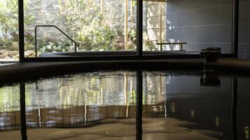 An indoor swimming pool with clear water, a bench, and a view of greenery outside.