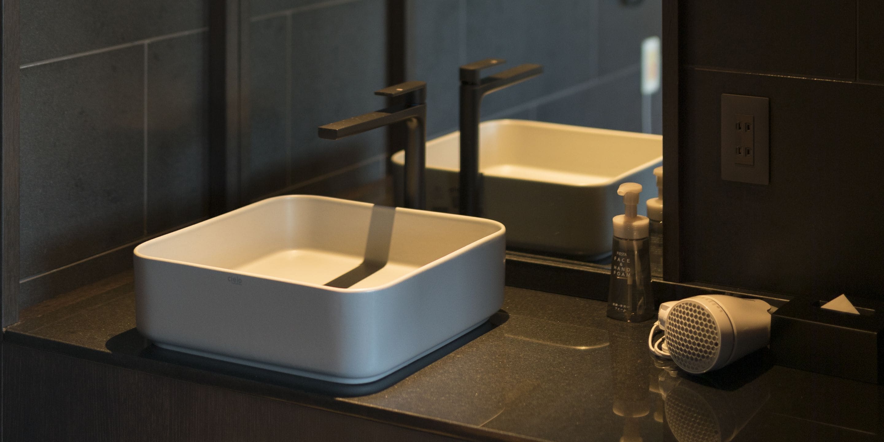 A bathroom with a white sink, a mirror, a hairdryer, and a bottle of hand soap.