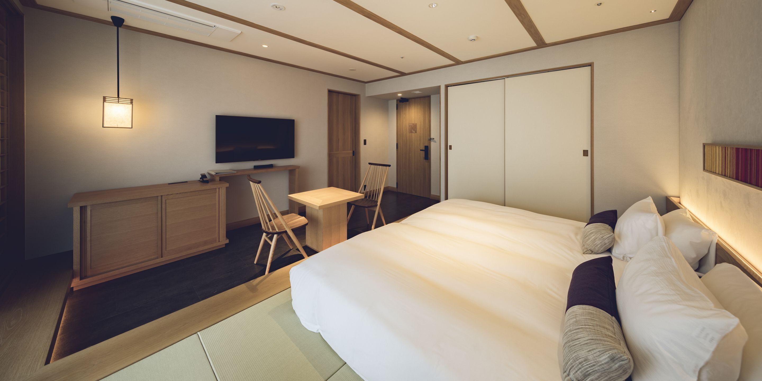 Una habitación de hotel moderna con una cama grande, un escritorio, una silla, un televisor y un armario.