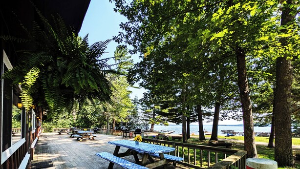A wooden deck with picnic tables and benches, overlooking a body of water. - Premium Amenities Included! Cabin 9 - POV Resort (Phelps)