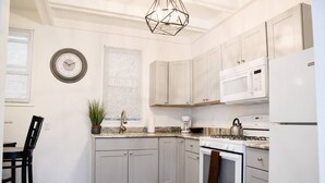 A kitchen with white cabinets, a microwave, stove, and a clock on the wall. - Bright 1BR Retreat | Near Downtown & Airport (Pittsburgh)