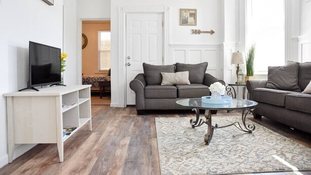 A living room with a grey sofa, a glass coffee table, and a white entertainment unit with a TV. - Bright 1BR Retreat | Near Downtown & Airport (Pittsburgh)
