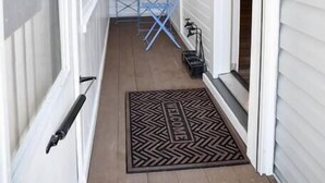 A narrow porch with a blue folding table and chairs, a welcome mat, and a door leading to the interior. - Bright 1BR Retreat | Near Downtown & Airport (Pittsburgh)