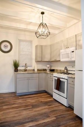 Une cuisine avec des meubles de couleur gris clair, un micro-ondes blanc, une cuisinière et un luminaire suspendu de forme géométrique.