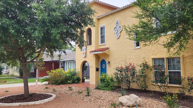 A yellow stucco building with a blue door, arched windows, and a decorative tile above the door. - Spacious (2/1, 1100 sqf) - 5 -15 minutes to Airport, Downtown, SeaWorld, etc. (San Antonio)