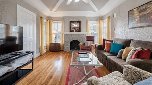 A living room with a fireplace, a ceiling fan, a television, and a sofa with cushions. - Spacious (2/1, 1100 sqf) - 5 -15 minutes to Airport, Downtown, SeaWorld, etc. (San Antonio)