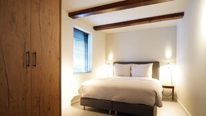 A bedroom with a large wooden wardrobe, a bed with a grey headboard, and two bedside lamps.