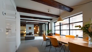 A modern dining area with a wooden table, orange chairs, and a large window providing natural light.