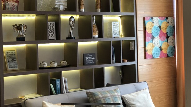 Un soggiorno moderno con un divano, elementi decorativi e una libreria con scaffali illuminati.