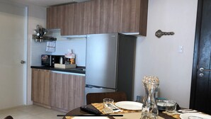 Una cucina compatta con mobili in legno, un frigorifero in acciaio inossidabile e un forno a microonde. È presente un tavolo da pranzo con un vaso, piatti e posate.