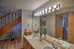 Bathroom features a dual sink vanity, large mirror, and wooden staircase.