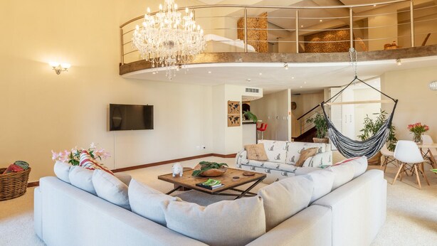 A spacious living room with a large sectional sofa, a wooden coffee table, a hanging chair, and a chandelier. - Uber Luxurious NYC-Style Penthouse, Two Minutes Walk from Long Street (Cape Town)