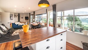 Une cuisine moderne avec un plan de travail en bois, un luminaire suspendu et une vue sur l’extérieur grâce à de grandes fenêtres.