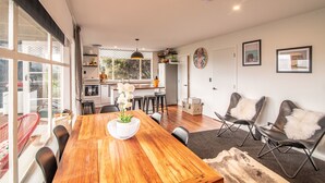 Une cuisine moderne avec des appareils électroménagers blancs, un coin repas avec une table en bois et des chaises noires, et un espace salon confortable avec des fauteuils en cuir et un plaid en fourrure.