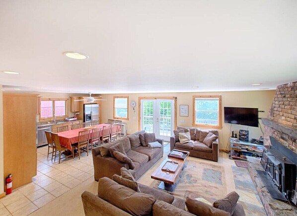 A spacious living room with a fireplace, a dining area with a red table, and a kitchen in the background. - Spacious and Comfortable home. Sleeps 8. 6 bedrooms. AC in all living areas. (West Dover)