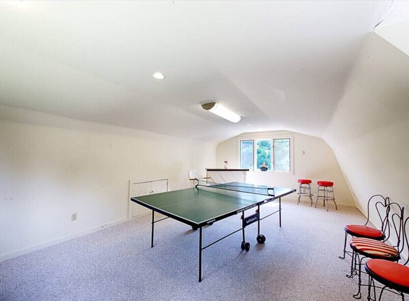 Una habitación con mesa de ping pong, dos taburetes y ventana con vistas.