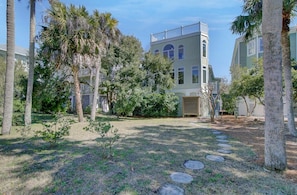 A building with a light green facade, a balcony on the upper floor, and a surrounding garden with palm trees and a stone pathway.