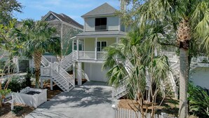 A two-story house with a balcony, surrounded by palm trees and a white picket fence.