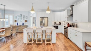 A modern kitchen with white cabinets, a central island with bar stools, stainless steel appliances, and pendant lighting.