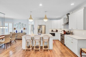 A modern kitchen with white cabinets, a central island with bar stools, stainless steel appliances, and pendant lighting.