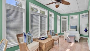 A sunroom with a ceiling fan, wicker furniture, and a bed with pillows.